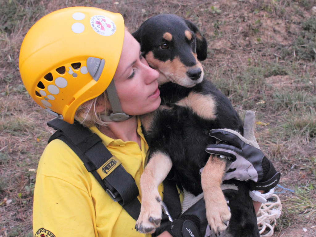 Ženski spasilac u uniformi Animal Rescue Serbia, u opremi, drži uz obraz tek spasenog psa.